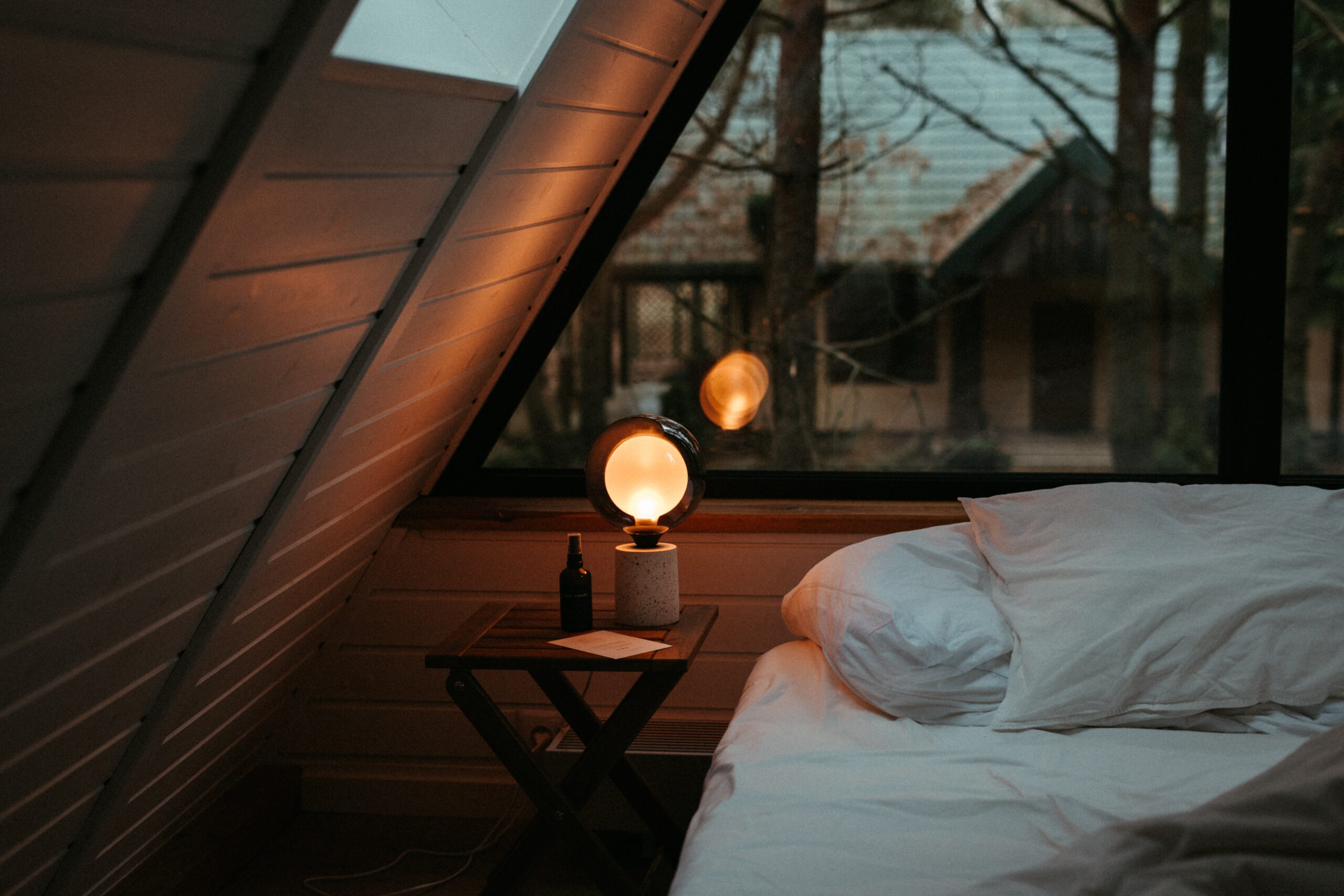 A cozy bed with a lamp on it, placed beside a window, offering a serene view.